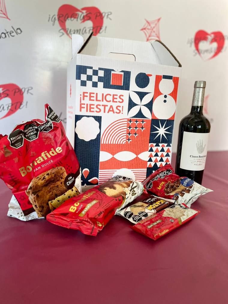 Caja de cartón navideña "¡Felices Fiestas!" con pan dulce, budín, turrón, chocolates y una botella de vino