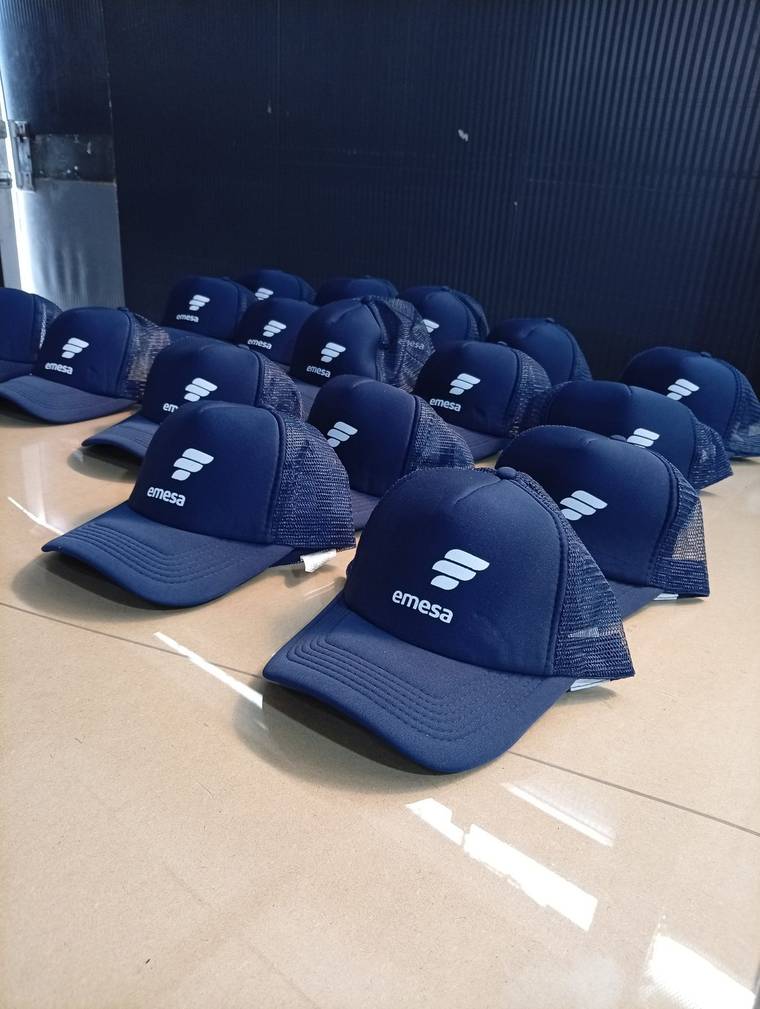 Gorras trucker azul marino con el logo de EMESA serigrafiado, alineadas en el taller